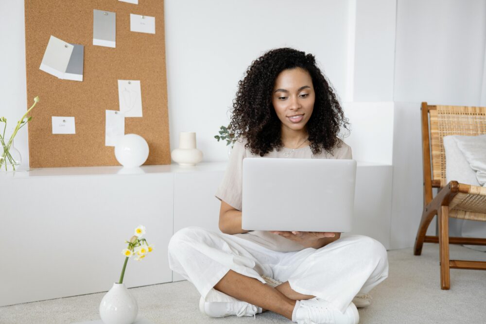 Woman working on a laptop while sitting on the floor in a bright minimalist room.
